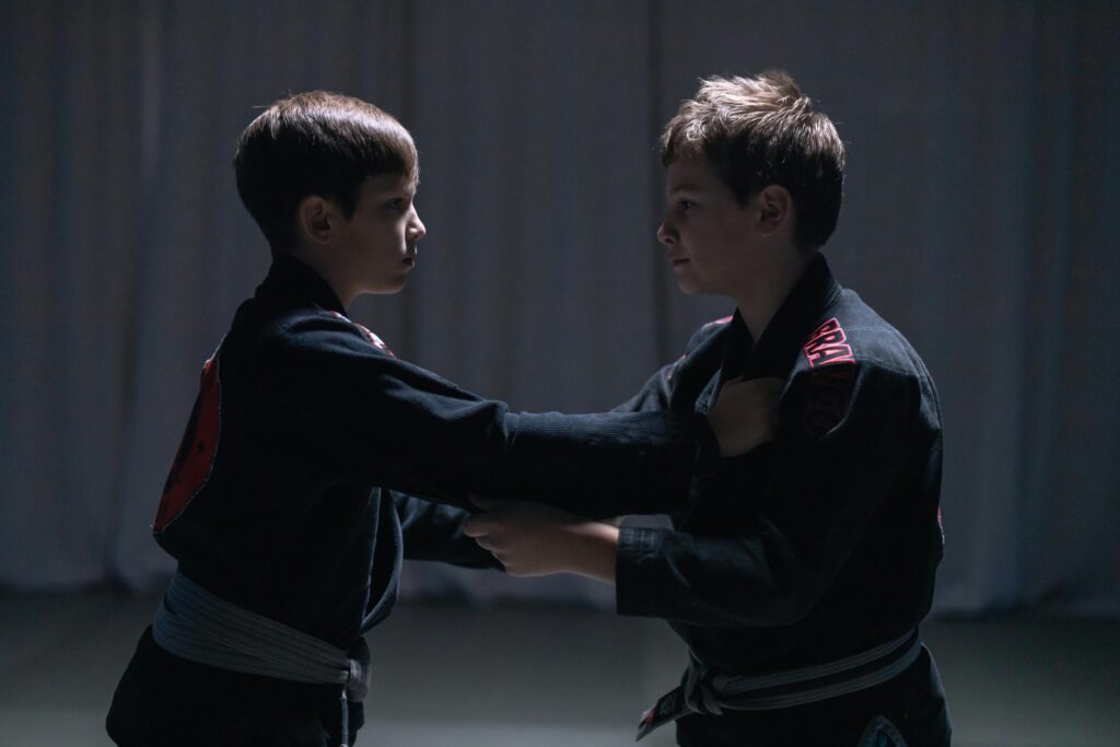 Two young jiu-jitsu practitioners in black gis, demonstrating a basic grappling technique.