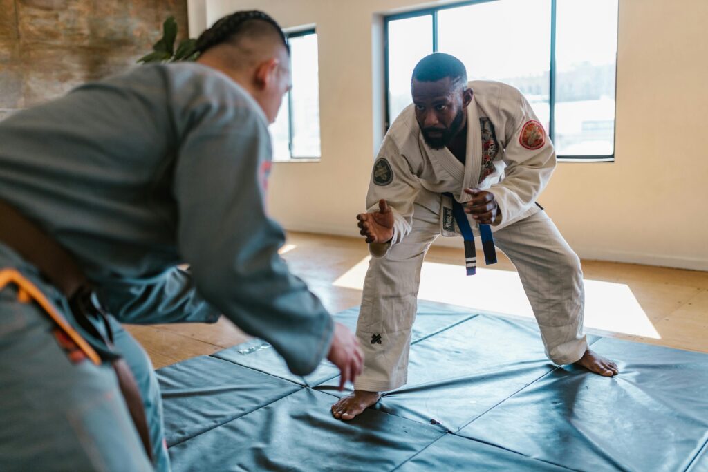 Two jiu-jitsu practitioners in gis, one with a blue belt and one with a brown belt, getting ready to demonstrating a basic grappling technique