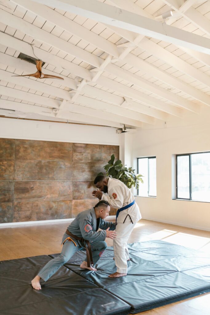 Two jiu-jitsu practitioners in gis, one with a blue belt and one with a brown belt, demonstrating a basic grappling technique